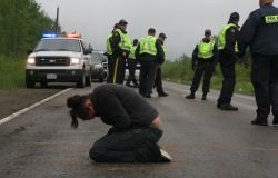 Susanne Patles in prayer, as New Brunswick RCMP confer. [Photo: M. Howe]