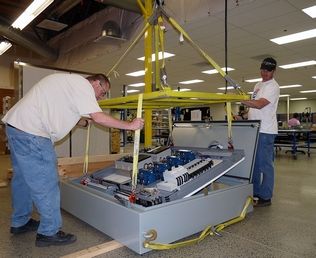 Kurt Batdorf / The Herald Business JournalProcess Solutions workers Bill Desmul (left) and Zach Barnes use a crane to lower a completed panel into an electrical service box at the company's Stanwood assembly plant.