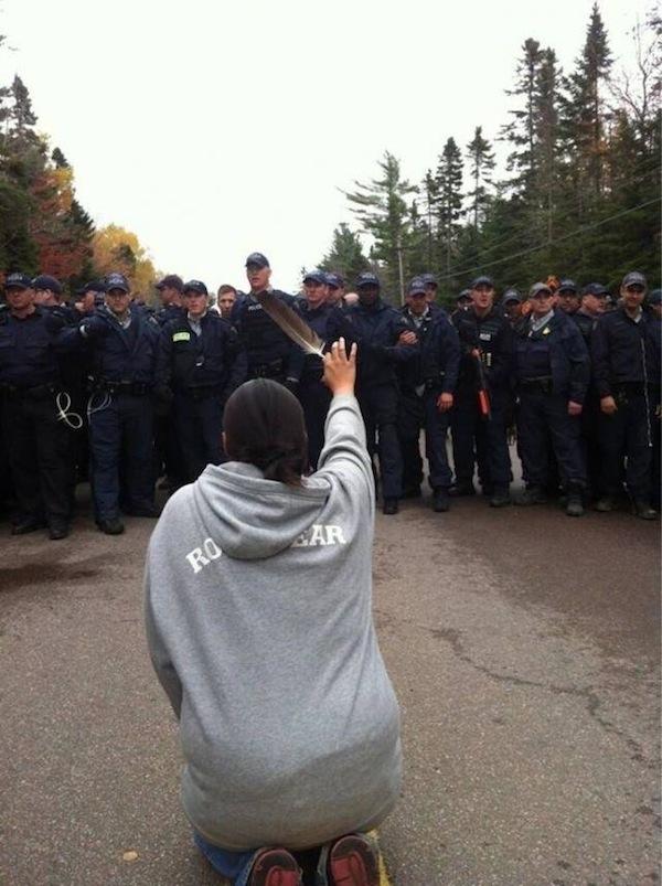 Courtesy Ossie Michelin, APTN National NewsThis photo of 28-year-old Amanda Polchies kneeling before Royal Canadian Mounted Police while brandishing an eagle feather during anti-fracking protests in New Brunswick has become iconic as a symbol of resistance to destructive industrial development—and of women's role in fighting for the water.