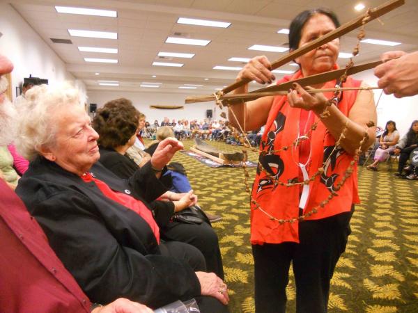 Richard WalkerSamish Nation cultural director Rosie Cayou James presents a string of smoked clams strung on sinew to Mary Jean Cahail, president of the San Juan Historical Society, June 28. The Old One can be seen in the background.