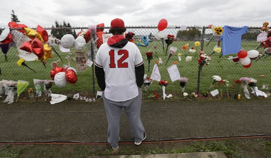 Brandon Bethers, 20, wears his Marysville Pilchuck High School baseball jersey as he views the growing memorial, Monday, Oct. 27, 2014, at the school in Marysville, Wash. On Friday, Oct. 24, 2014, student Jayson Fryberg opened fire in the school cafeteria, killing a fellow student and injuring others before taking his own life. A third student died Sunday night of her injuries.The school will be closed all week. (AP Photo/Ted S. Warren)