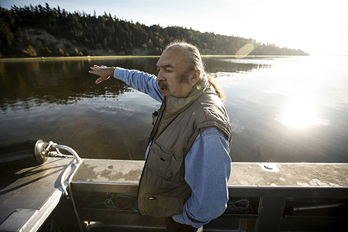 From a research boat on Oct. 12, Tulalip Tribes treaty rights commissioner Terry Williams points out a steep hillside near Mission Beach that has been gradually eroding for years. (Ian Terry / The Herald)